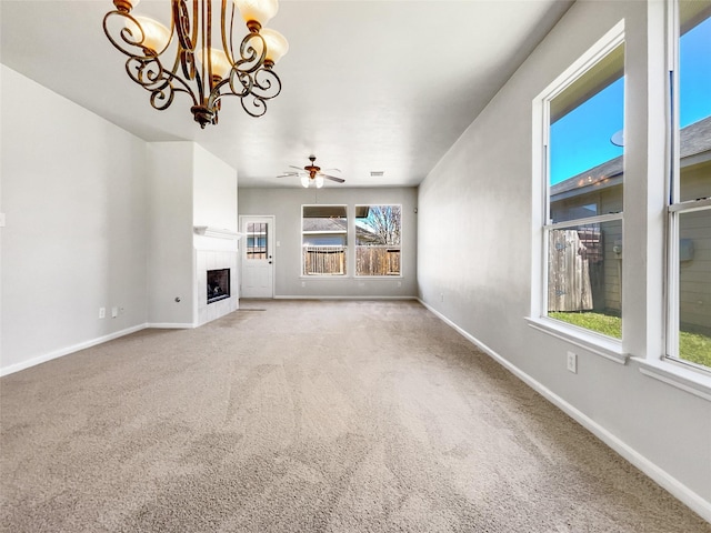 unfurnished living room with ceiling fan with notable chandelier, a fireplace, baseboards, and carpet