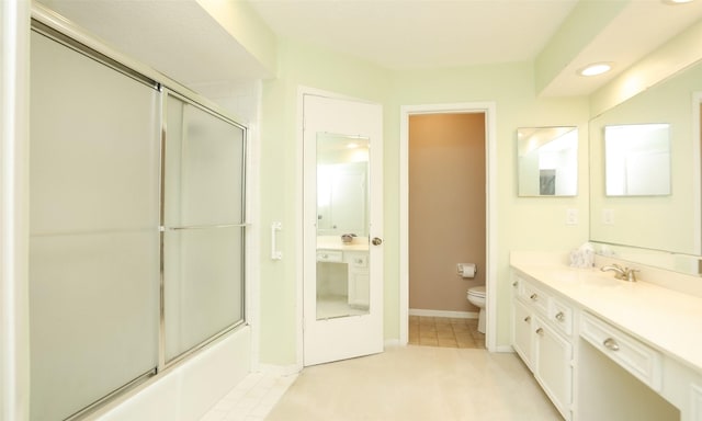 bathroom featuring toilet, combined bath / shower with glass door, vanity, tile patterned flooring, and baseboards