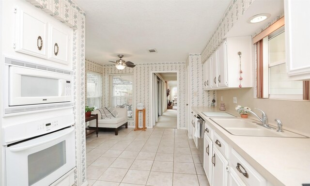 kitchen with white appliances, a sink, visible vents, white cabinets, and wallpapered walls