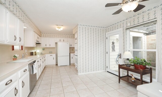 kitchen featuring wallpapered walls, white cabinets, freestanding refrigerator, light countertops, and stainless steel dishwasher