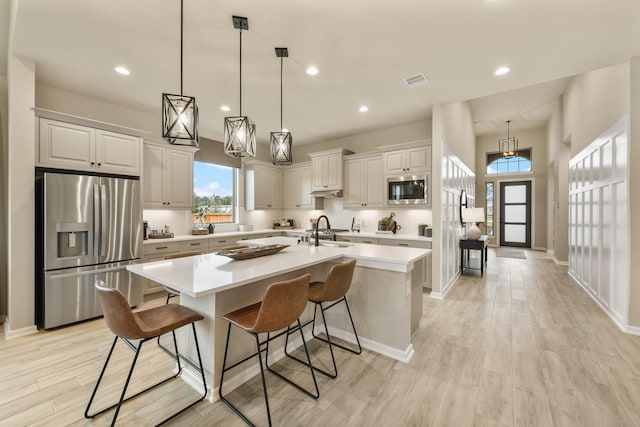 kitchen with a kitchen island with sink, a sink, light countertops, appliances with stainless steel finishes, and light wood finished floors