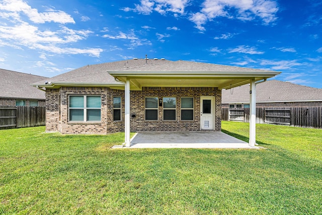 back of house with roof with shingles, brick siding, a patio, a lawn, and a fenced backyard