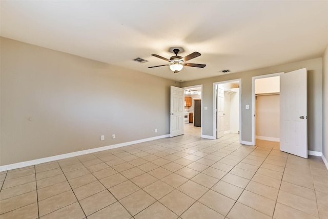 unfurnished bedroom featuring a walk in closet, visible vents, baseboards, and light tile patterned flooring