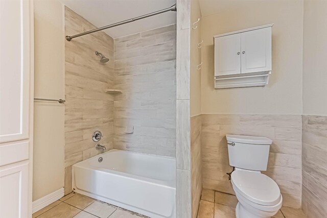 full bathroom with toilet, a wainscoted wall, tile patterned flooring, tub / shower combination, and tile walls