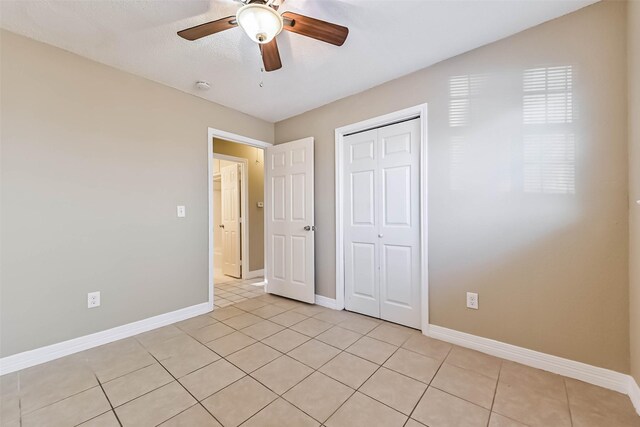 unfurnished bedroom featuring light tile patterned floors, ceiling fan, baseboards, and a closet