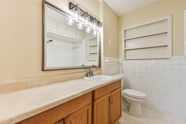 bathroom with toilet, vanity, tile walls, wainscoting, and tile patterned floors