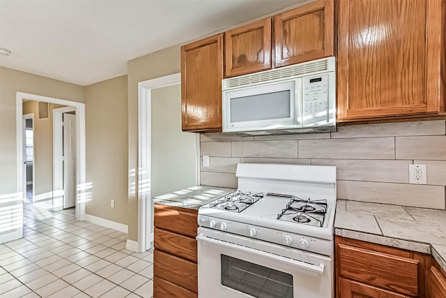 kitchen with white appliances, baseboards, tile countertops, brown cabinets, and backsplash