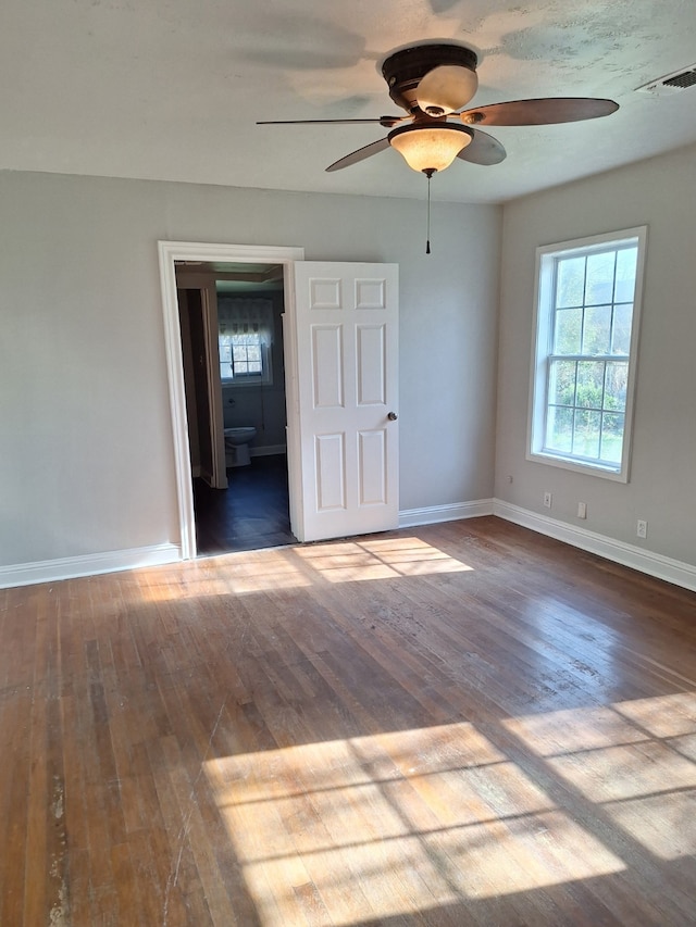 unfurnished bedroom featuring visible vents, hardwood / wood-style flooring, connected bathroom, baseboards, and ceiling fan