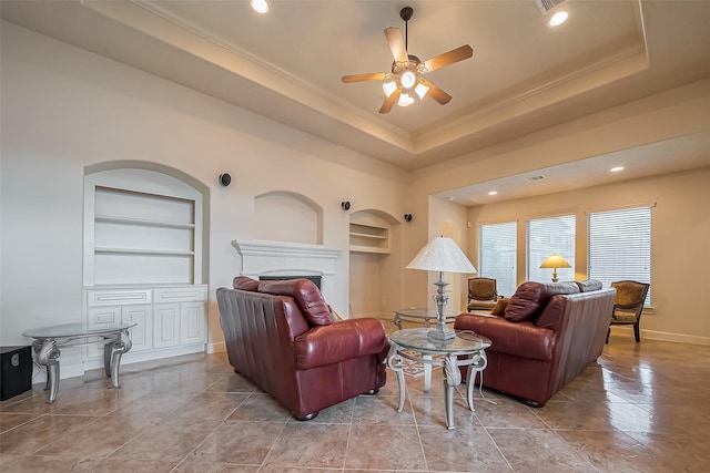 living room with built in shelves, a raised ceiling, a ceiling fan, a fireplace, and baseboards