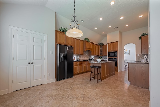 kitchen featuring brown cabinetry, a kitchen island, arched walkways, black appliances, and a kitchen bar