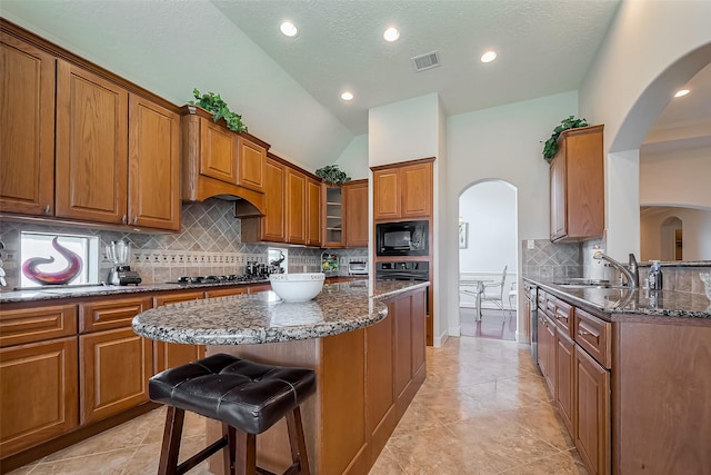 kitchen with visible vents, dark stone counters, arched walkways, brown cabinetry, and black microwave