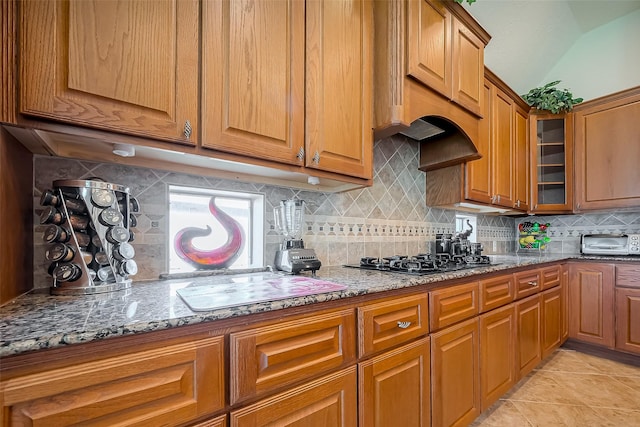 kitchen featuring brown cabinetry, stone counters, decorative backsplash, black gas cooktop, and glass insert cabinets