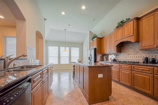 kitchen with a center island, vaulted ceiling, dark stone countertops, appliances with stainless steel finishes, and a sink