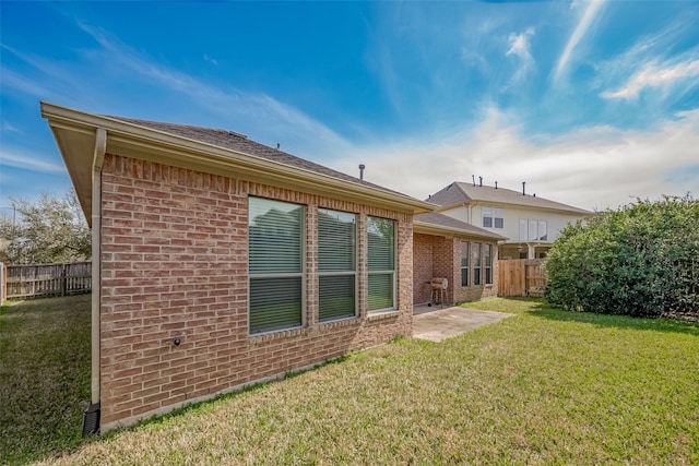 rear view of property featuring brick siding, a yard, and fence