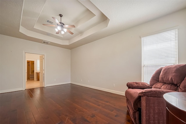 living area featuring a tray ceiling, visible vents, dark wood-style flooring, and a ceiling fan