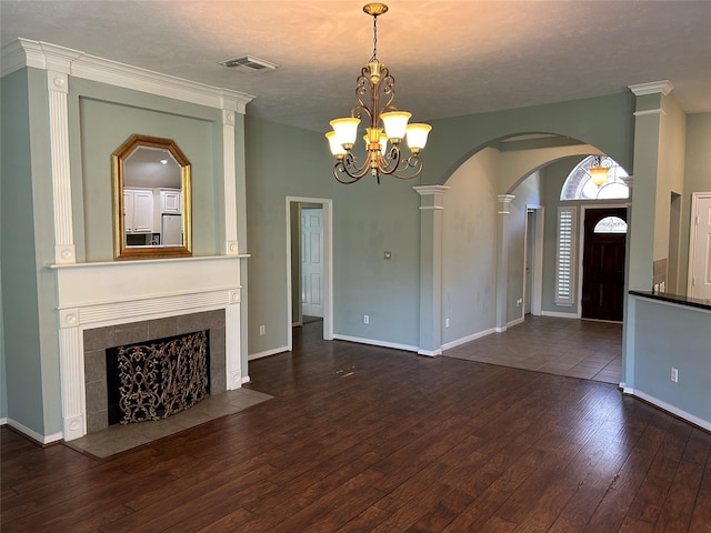 unfurnished living room with hardwood / wood-style flooring, visible vents, baseboards, a tiled fireplace, and decorative columns