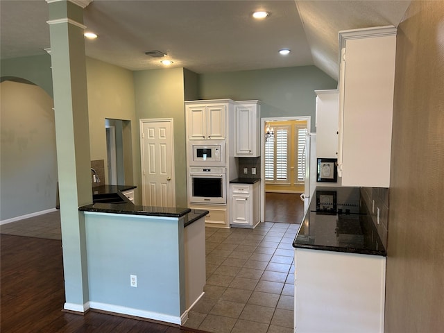 kitchen with white microwave, oven, dark tile patterned flooring, a sink, and white cabinets