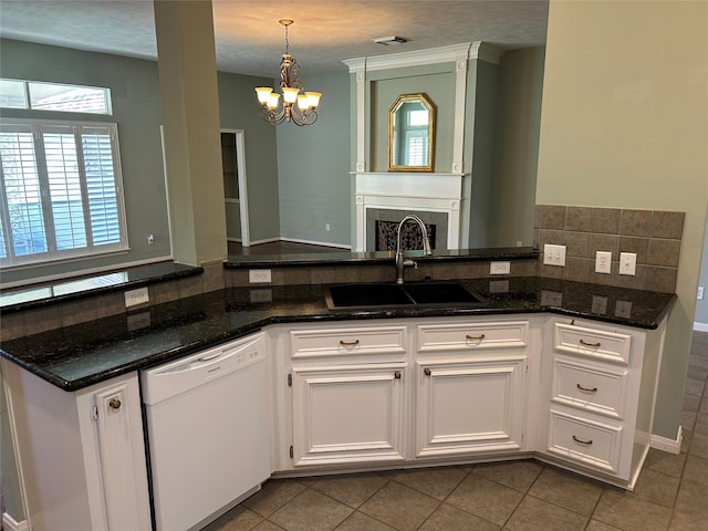 kitchen featuring white dishwasher, a sink, white cabinets, backsplash, and dark stone countertops