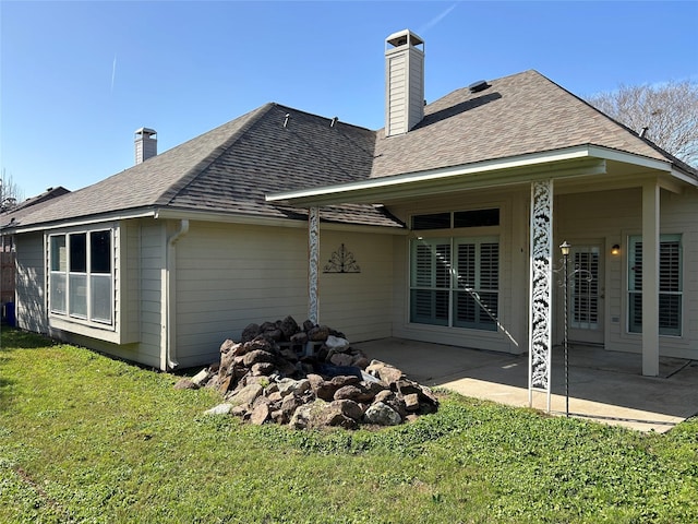 rear view of house with a patio area, roof with shingles, a yard, and a chimney