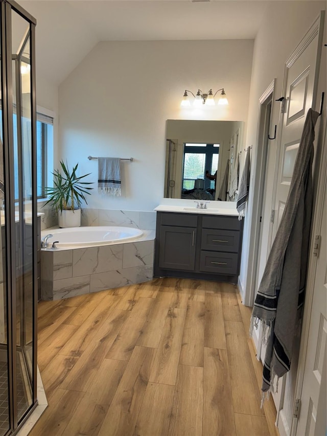 bathroom featuring a stall shower, lofted ceiling, wood finished floors, vanity, and a bath