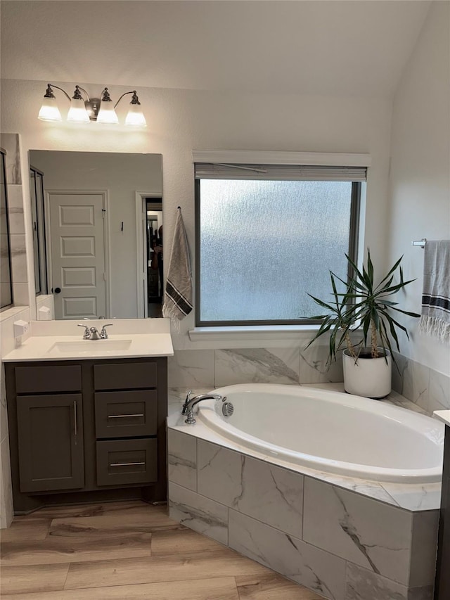 bathroom with a garden tub, plenty of natural light, vanity, and wood finished floors