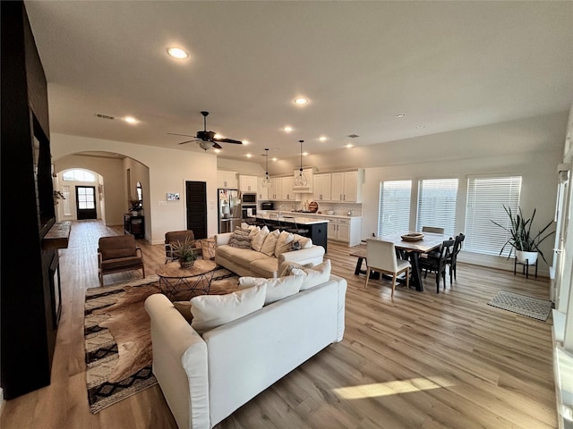 living room with arched walkways, light wood-style flooring, baseboards, and recessed lighting