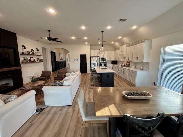 dining space featuring visible vents, arched walkways, lofted ceiling, light wood-type flooring, and a fireplace