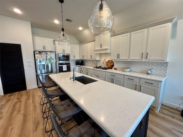 kitchen with visible vents, decorative backsplash, appliances with stainless steel finishes, a kitchen breakfast bar, and a sink