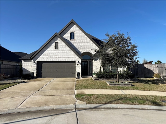 french country style house featuring a garage, fence, concrete driveway, and brick siding