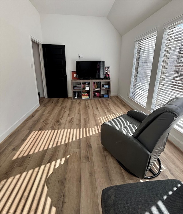 living room featuring vaulted ceiling, baseboards, and wood finished floors