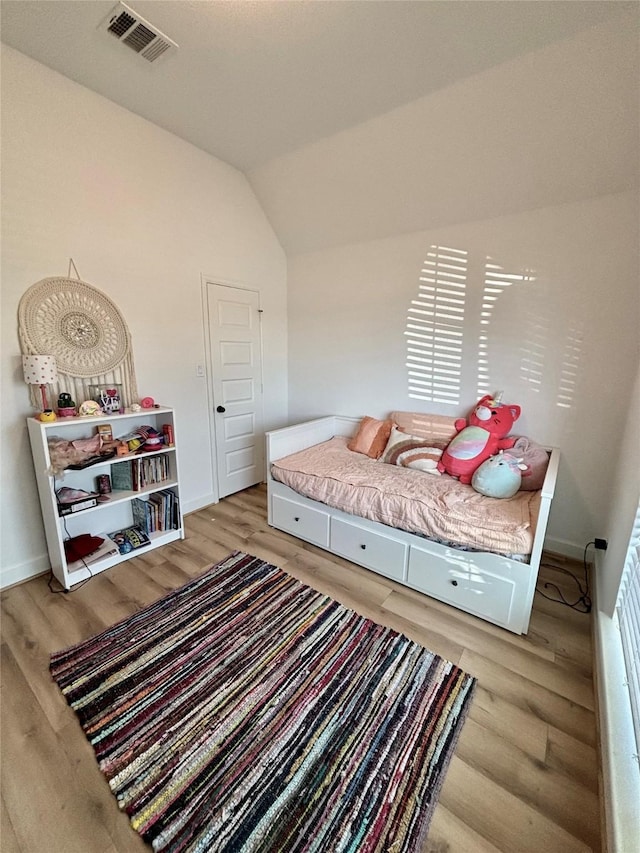 bedroom with vaulted ceiling, wood finished floors, visible vents, and baseboards