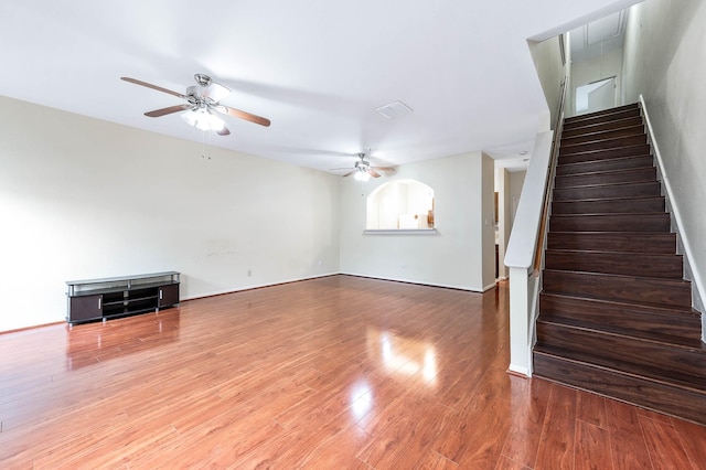 unfurnished living room featuring a ceiling fan, visible vents, stairway, and wood finished floors