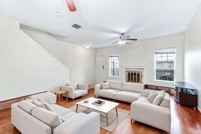 living area featuring ceiling fan, a fireplace, visible vents, baseboards, and light wood-type flooring