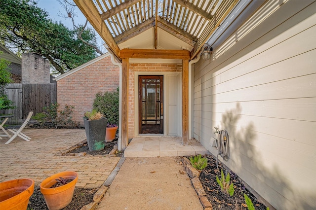 property entrance with a patio area, a balcony, brick siding, and fence