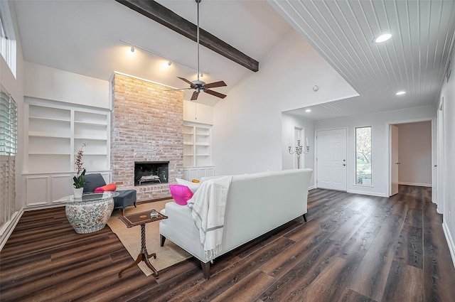 living area featuring beamed ceiling, built in features, dark wood finished floors, a fireplace, and ceiling fan