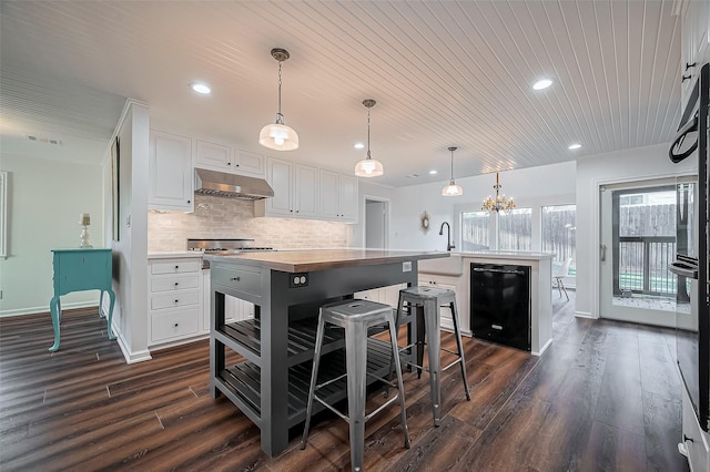 kitchen with visible vents, under cabinet range hood, a kitchen island, backsplash, and dishwasher