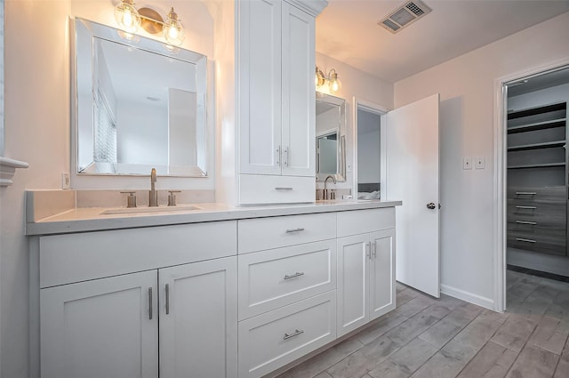 full bathroom featuring visible vents, a sink, wood finished floors, double vanity, and baseboards