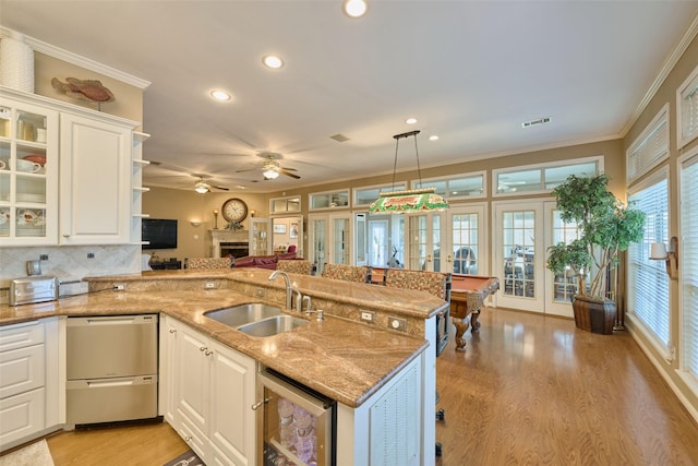 kitchen featuring crown molding, light wood-style flooring, a peninsula, french doors, and a sink