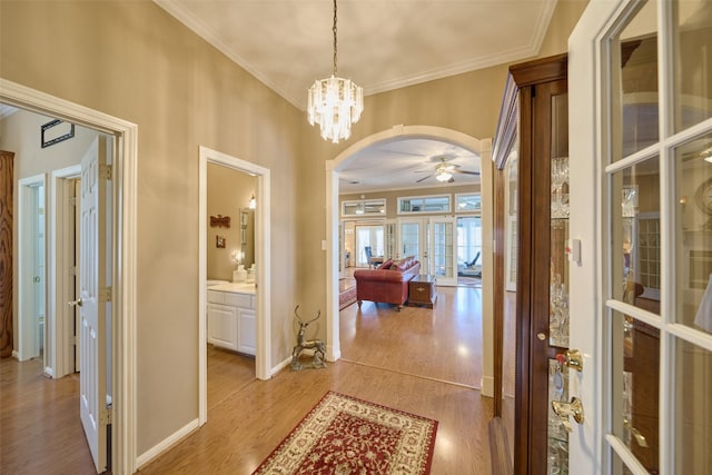 hallway featuring light wood-type flooring, arched walkways, ornamental molding, and french doors