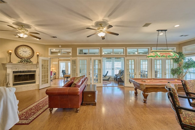 living area with visible vents, ornamental molding, wood finished floors, a high end fireplace, and french doors