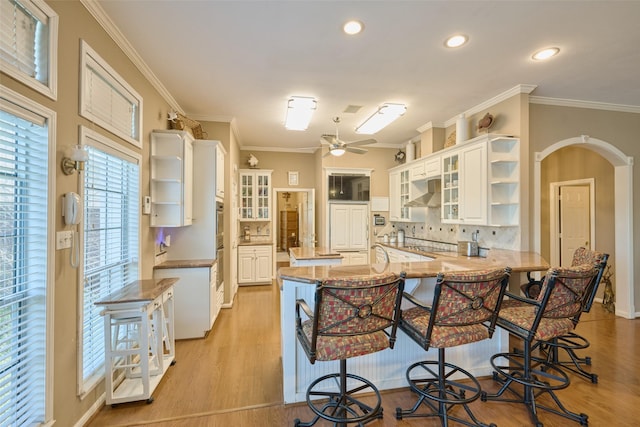 kitchen with open shelves, a peninsula, arched walkways, decorative backsplash, and a kitchen bar