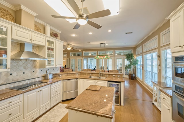 kitchen featuring a peninsula, ornamental molding, stainless steel appliances, wine cooler, and wall chimney range hood