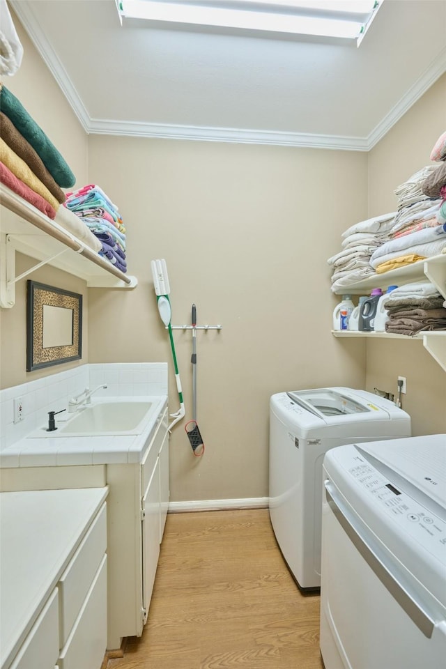 washroom with light wood-type flooring, a sink, cabinet space, separate washer and dryer, and crown molding