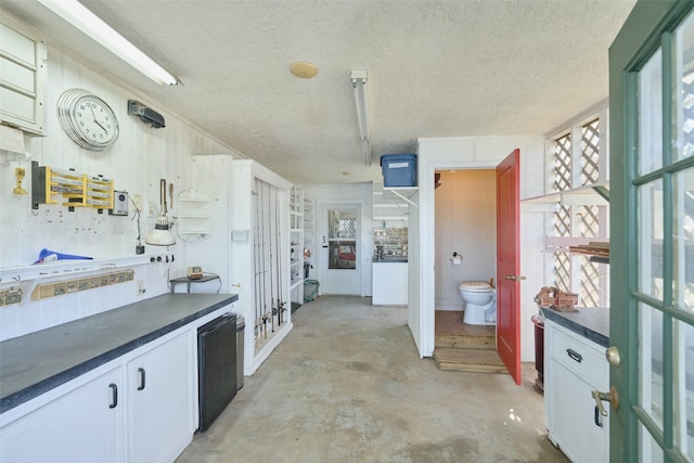 kitchen featuring dark countertops, a textured ceiling, white cabinetry, fridge, and unfinished concrete floors