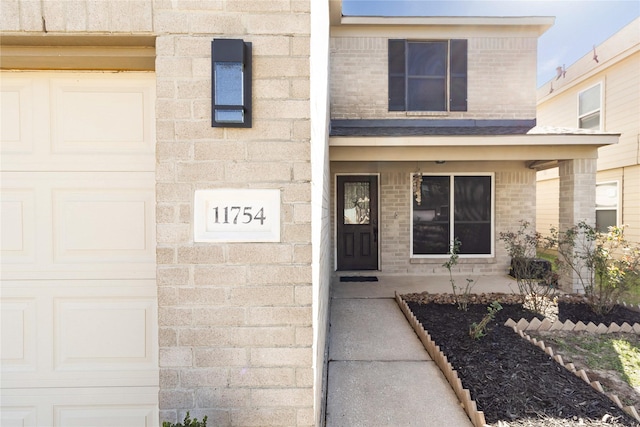 property entrance with a porch, brick siding, and an attached garage