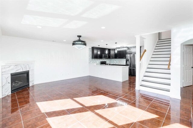 unfurnished living room with a notable chandelier, a premium fireplace, stairway, and recessed lighting