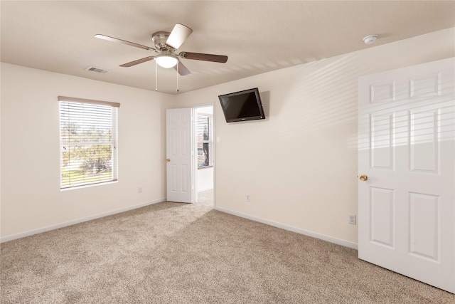 spare room featuring light carpet, ceiling fan, visible vents, and baseboards