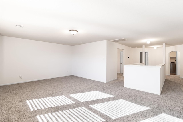 spare room featuring arched walkways, washer / clothes dryer, light carpet, and baseboards