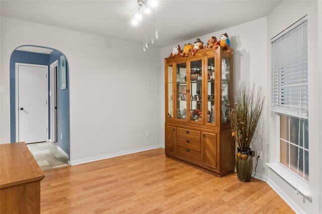 empty room featuring arched walkways, baseboards, and light wood-style floors