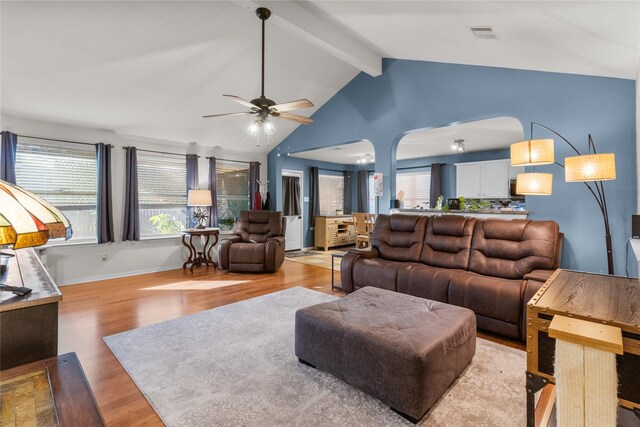 living area with light wood-type flooring, visible vents, a ceiling fan, baseboards, and vaulted ceiling with beams